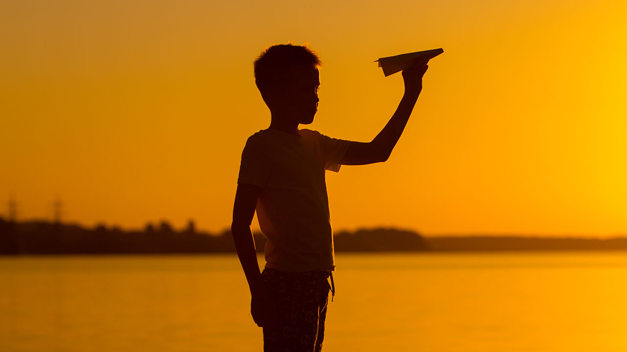 Boy, paper plane and sunset